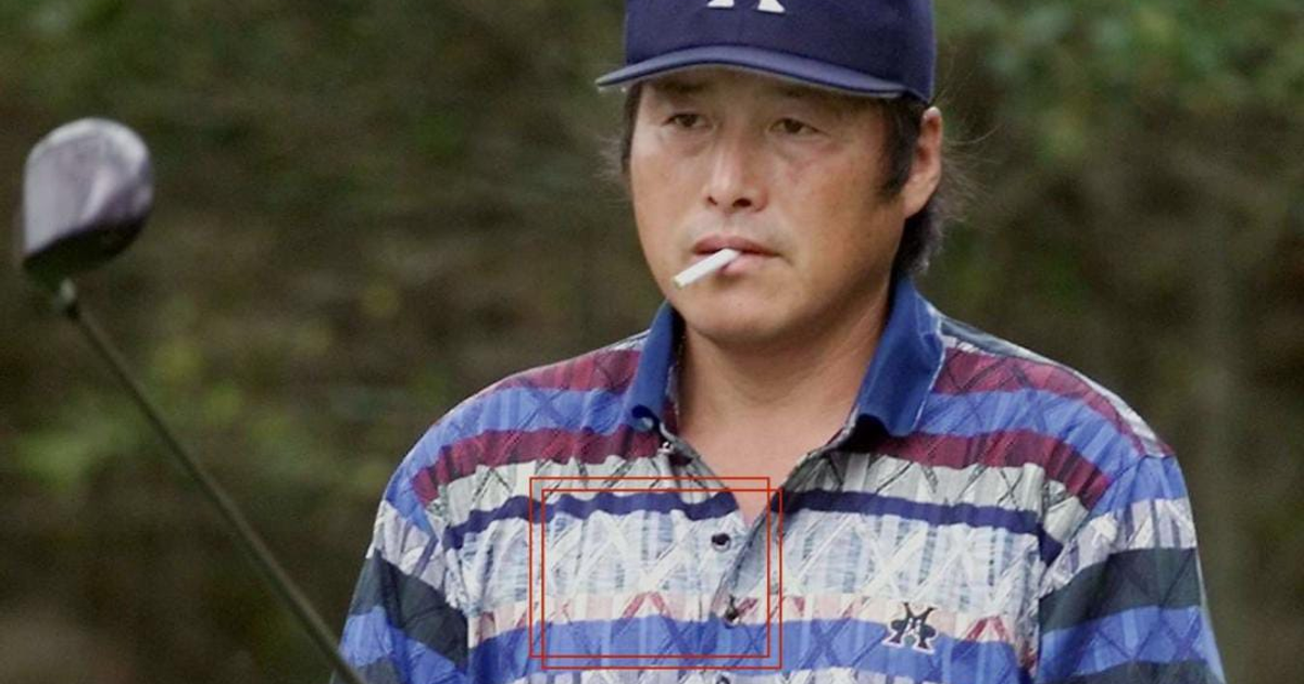 Hombre con gorra y camisa a rayas sostiene un cigarrillo, palo de golf detrás.