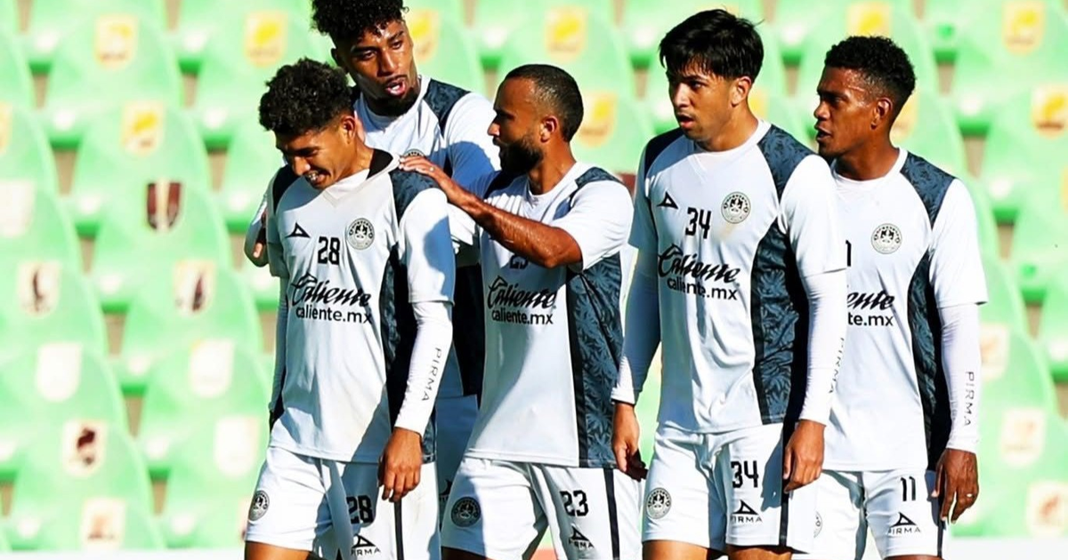 Jugadores de fútbol de Mazatlán FC celebrando en el Estadio TSM durante un amistoso contra Santos Laguna, con gradas verdes al fondo.