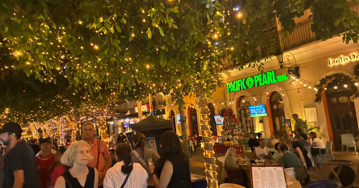 Personas disfrutando de una noche iluminada en la plazuela Machado, Mazatlán; luces, árboles y restaurante en el fondo.