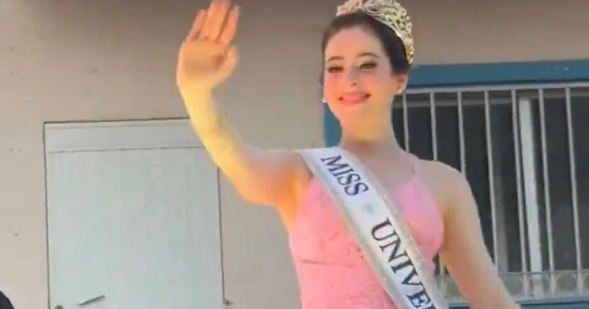 Joven en vestido rosa con tiara y banda 'MISS UNIVERSE' sonriendo y saludando