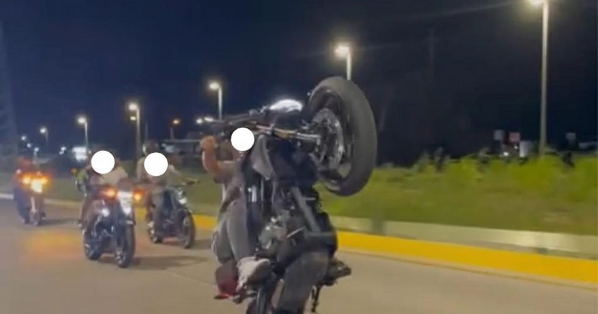 Motociclistas en la noche, uno haciendo wheelie, carretera iluminada
