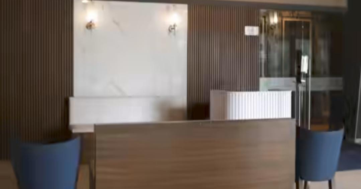 Recepción moderna en Murmullos Mazatlán con mostrador, paneles de madera y silla azul bajo una iluminación cálida.