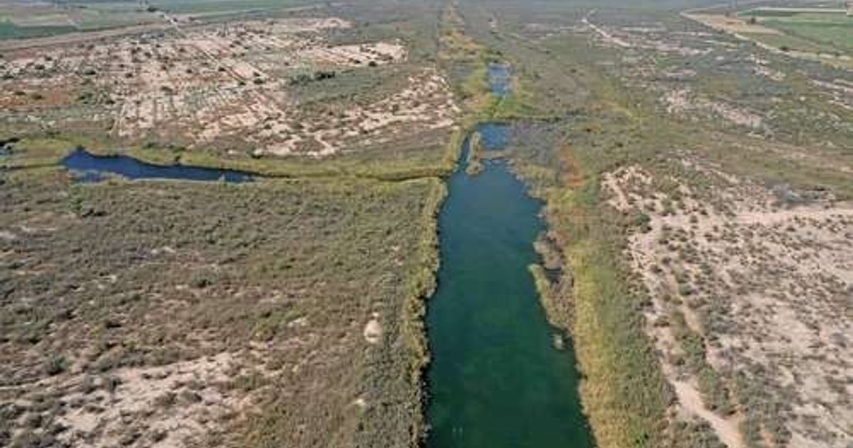 Vista aérea de un río en un terreno árido rodeado de vegetación y terrenos de cultivo.