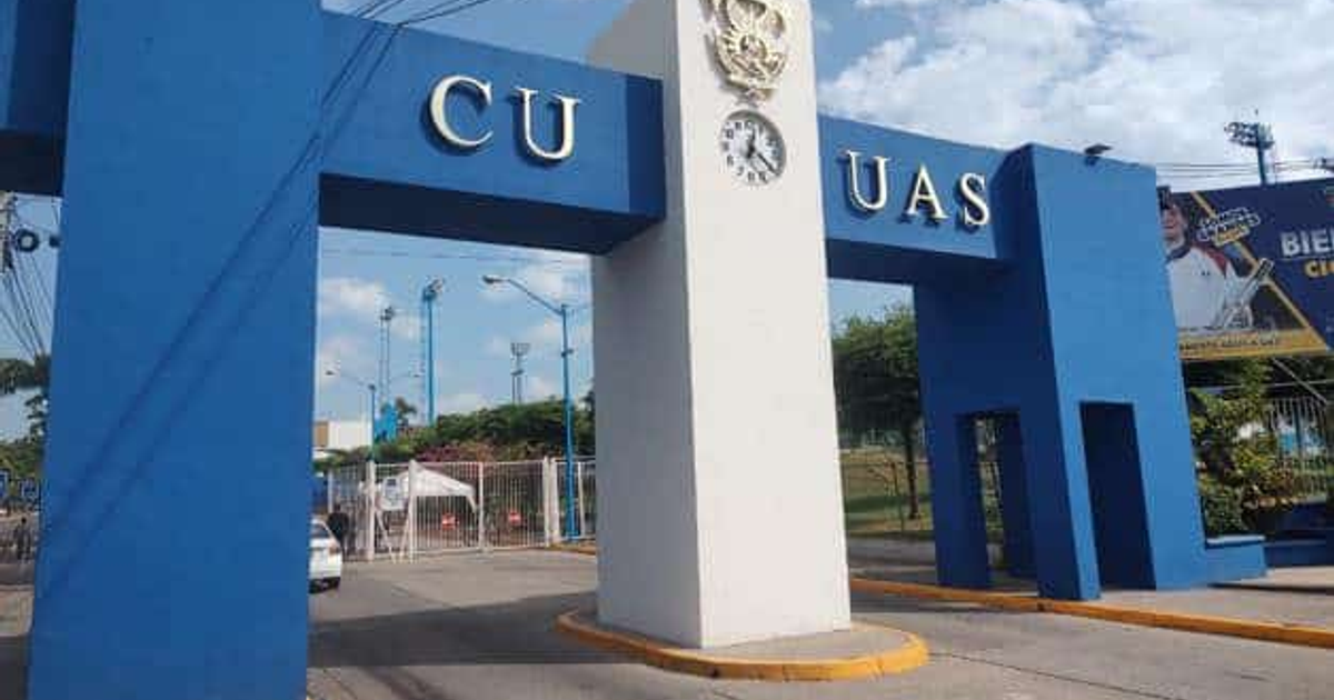 Fotografía de la entrada de la Universidad Autónoma de Sinaloa con las letras 'CU UAS' en azul, destacando un reloj y un escudo.