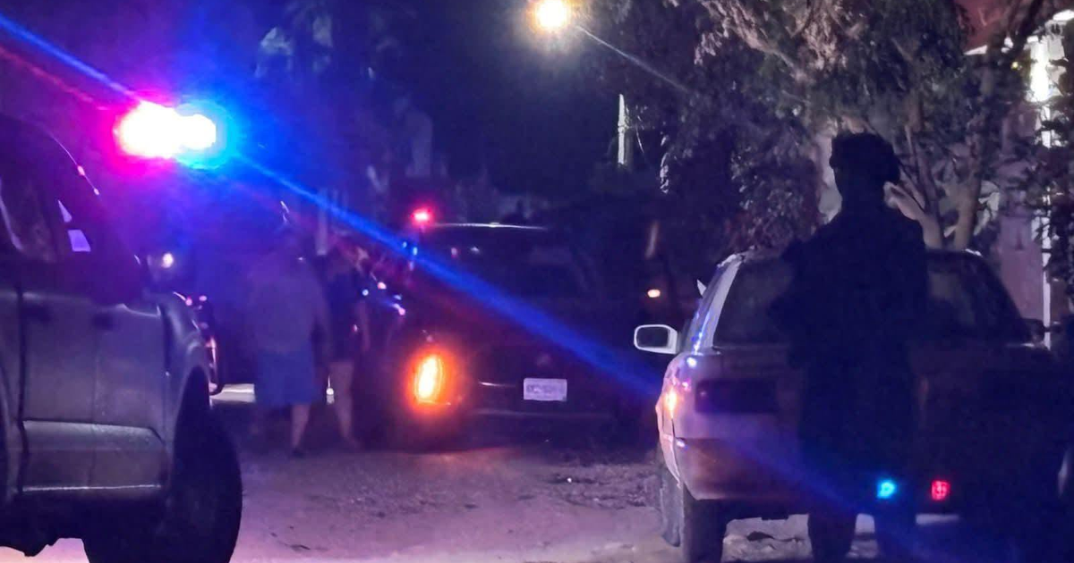 Luces intermitentes iluminan la noche en una carretera, mostrando autos detenidos y figuras humanas sugiriendo una emergencia.