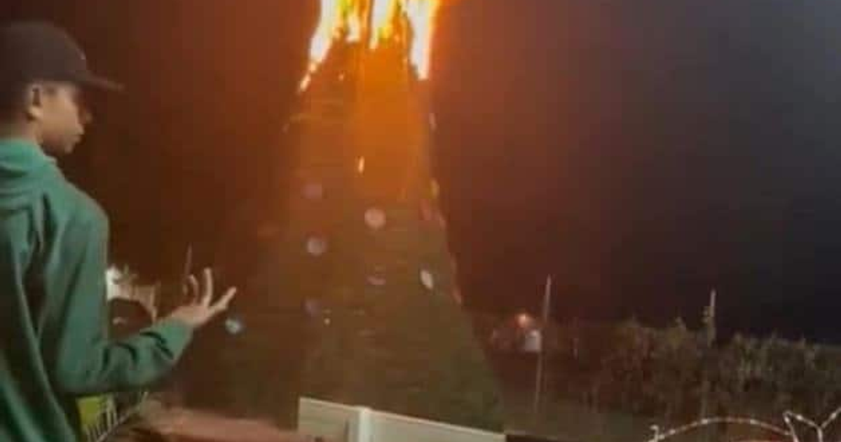 Árbol de Navidad en llamas en Caimanero, Sinaloa, con una persona observando de espaldas, una noche sin lesionados tras incidente de pirotecnia.