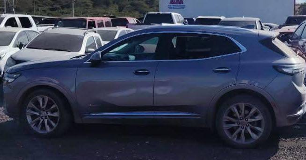 Camioneta gris SUV estacionada en área de desguace con coches blancos y de otros colores a su alrededor.