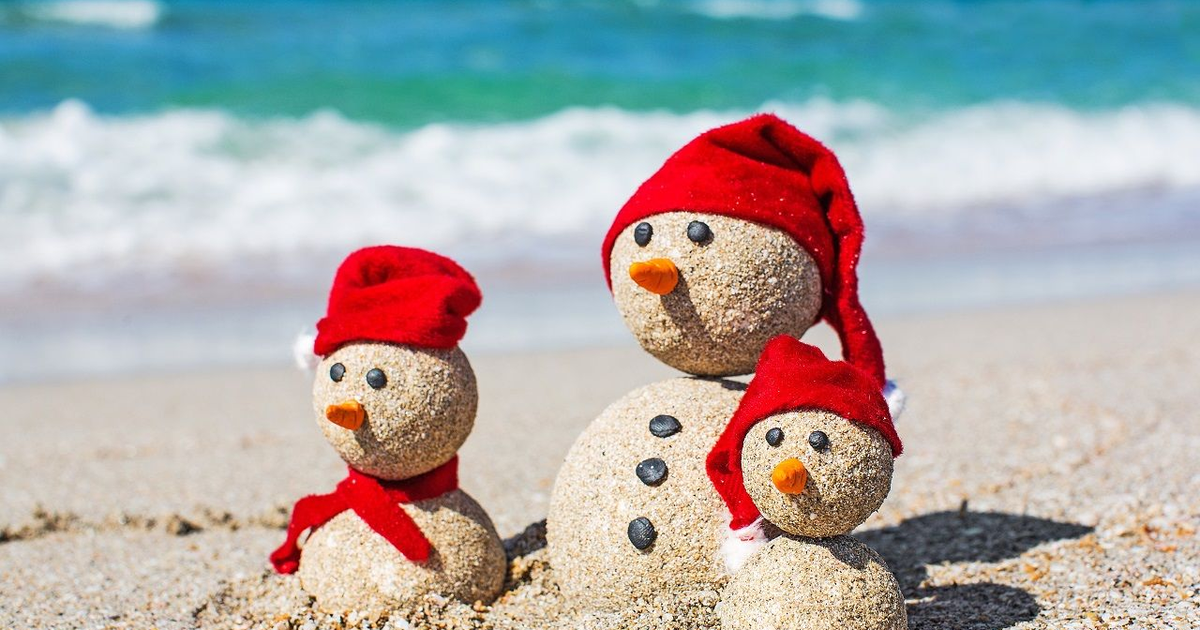 Muñecos de nieve de arena en la playa de Los Mochis, con bufandas y gorros rojos, frente al mar.
