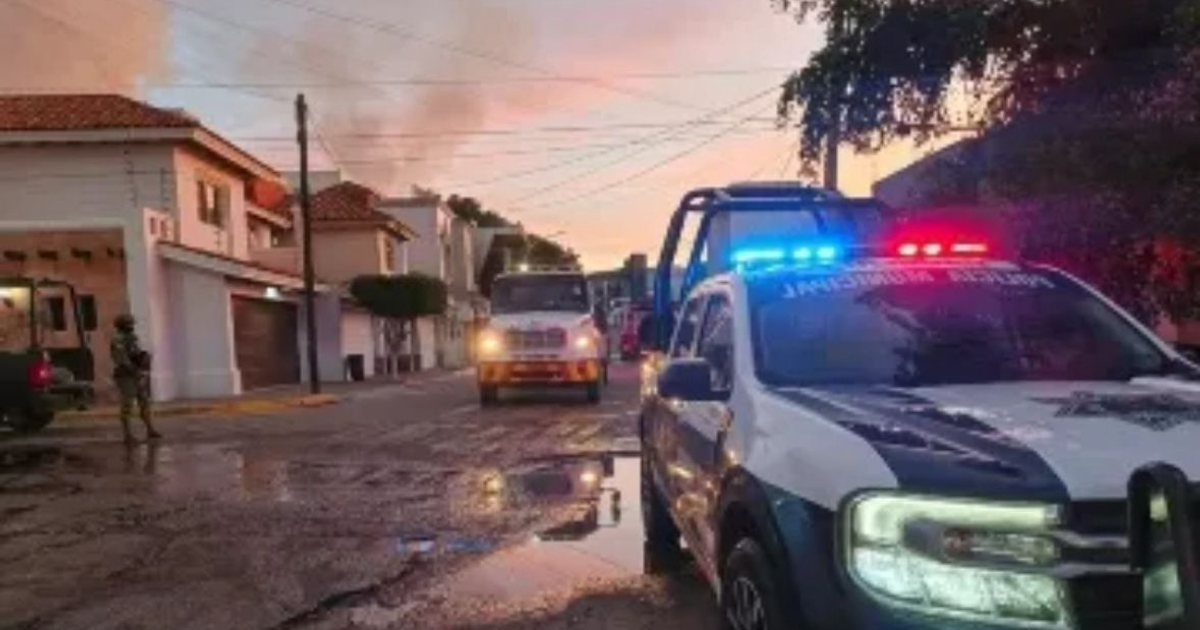 Calle en Culiacán con un operativo policial y humo visible al fondo al amanecer o atardecer.