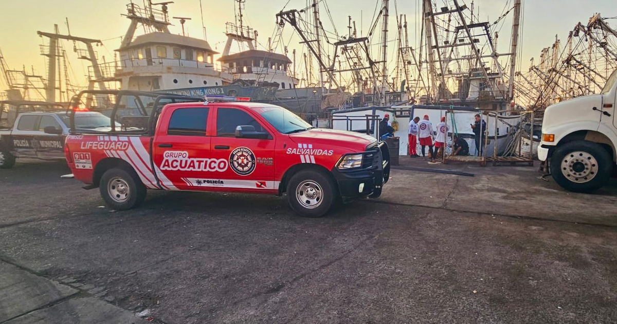 Escena de amanecer en el puerto de Mazatlán con vehículos de emergencia y barcos pesqueros.