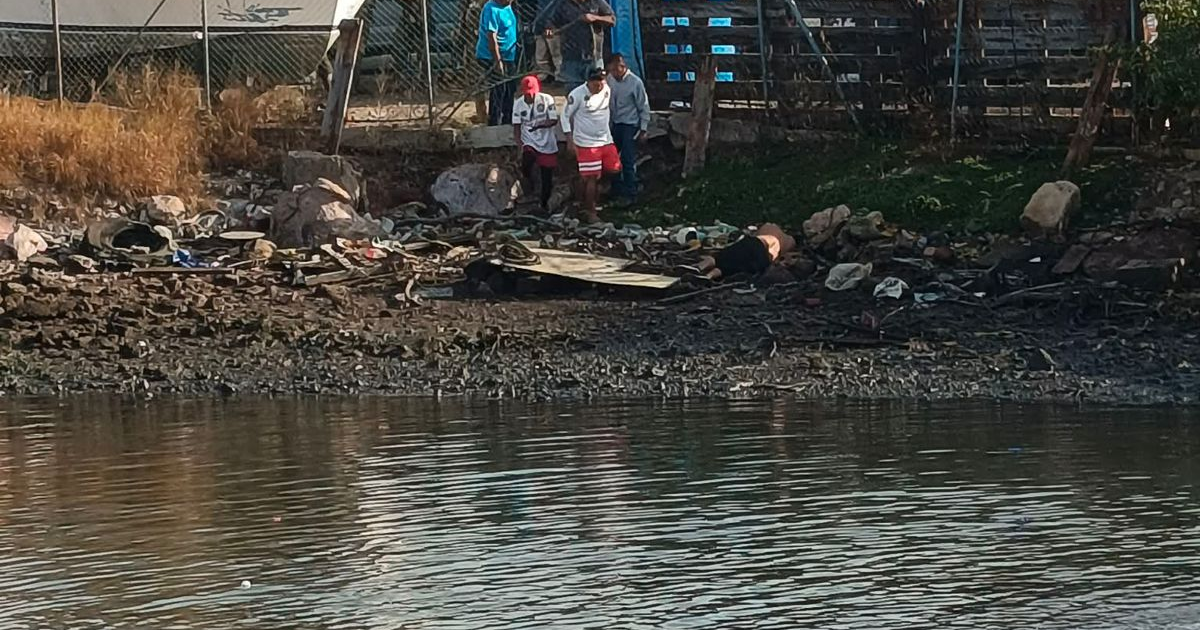 Vista de la orilla del río en Mazatlán con personas y desechos, relacionada con un rescate acuático.