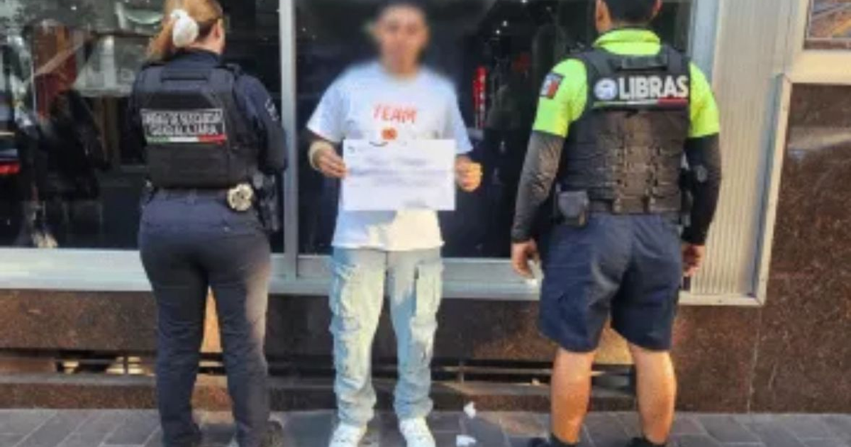 Agentes de policía interactuando con una persona sosteniendo un cartel en una calle urbana.