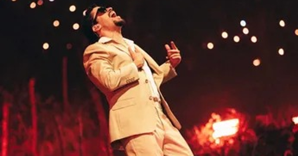 Cantante en traje claro actúa apasionadamente en un escenario iluminado con luces brillantes.