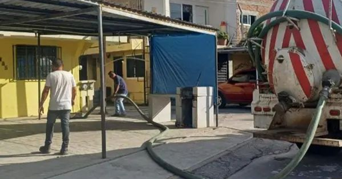 Camión mezclador de cemento rojo y blanco con trabajadores gestionando una obstrucción de drenaje al aire libre