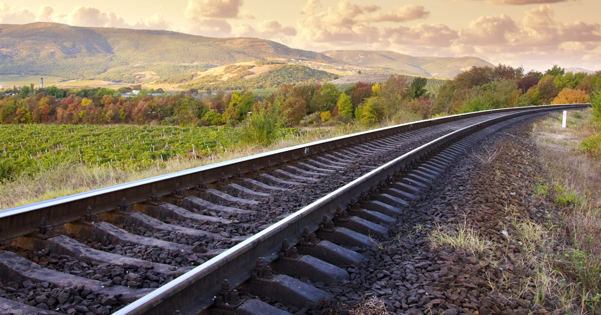 Tranquila vía de tren hacia montañas con viñedos a la izquierda durante el otoño.