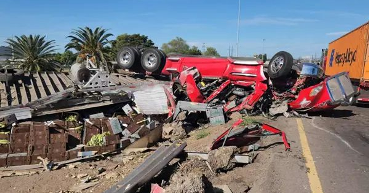 Camión volcado junto a una carretera con escombros y un contenedor de fondo.
