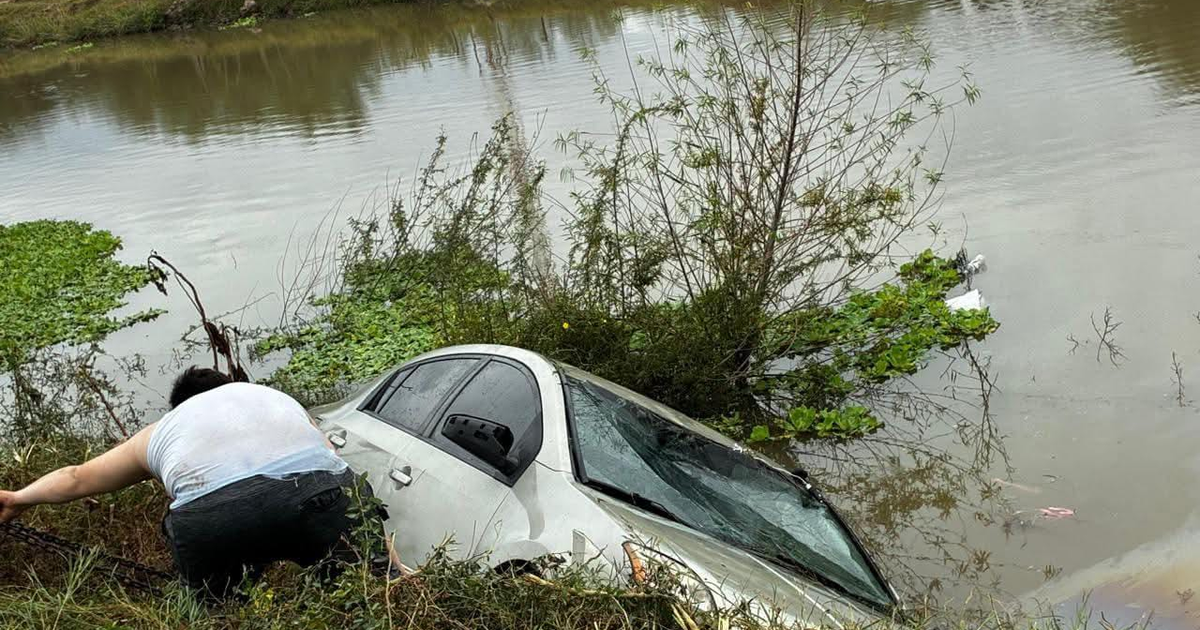 Automóvil parcialmente sumergido en un canal con persona al lado intentando rescatarlo. Nissan Sentra en canal lateral 18, Los Mochis.