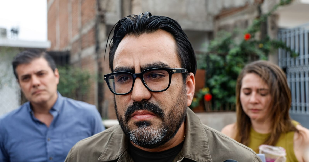 Hombre con gafas en primer plano en un evento urbano con fondos de ladrillo y plantas.