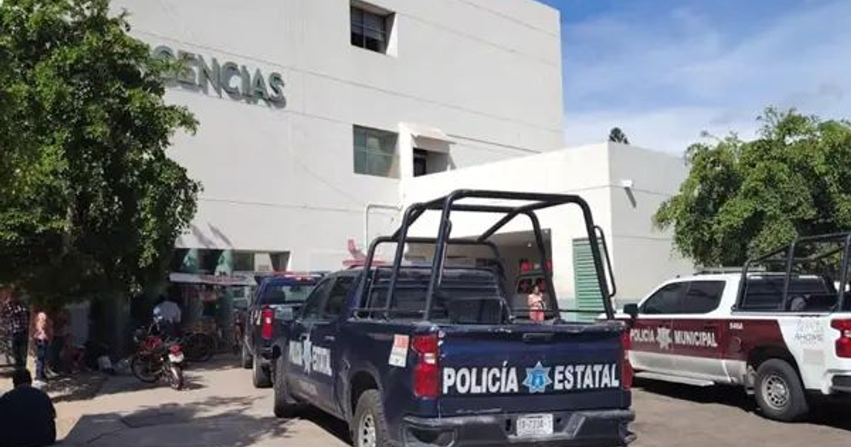 Edificio de urgencias con vehículos policiales y personas presentes, reflejando una escena de emergencia médica y seguridad.