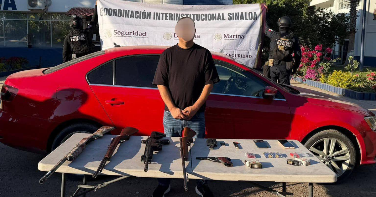 Hombre detenido frente a automóvil rojo con arsenal decomisado en Culiacán bajo la vista de autoridades de seguridad.