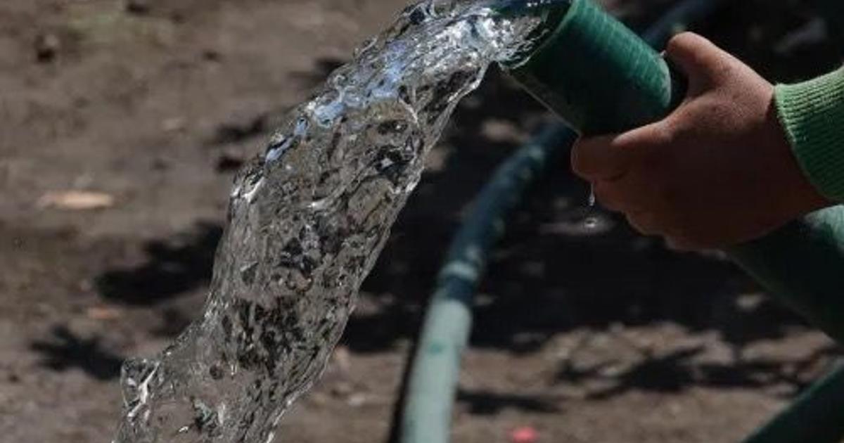 Manguera liberando agua sostenida por una mano sobre suelo