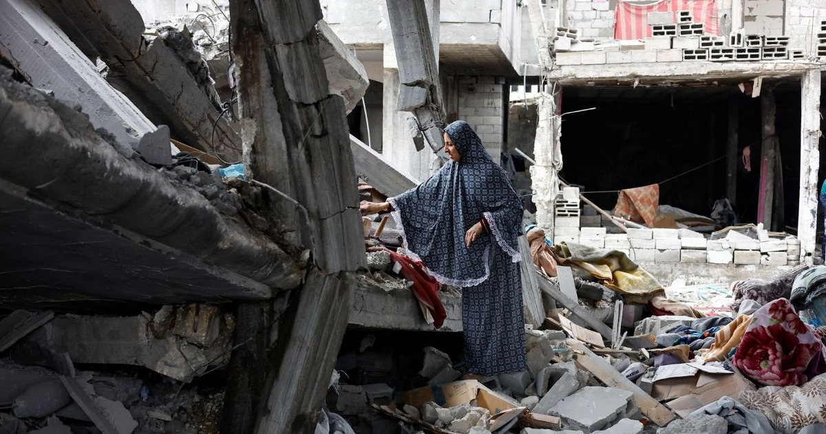 Mujer en zona de desastre en Gaza revisando escombros, reflejando la crisis humanitaria.