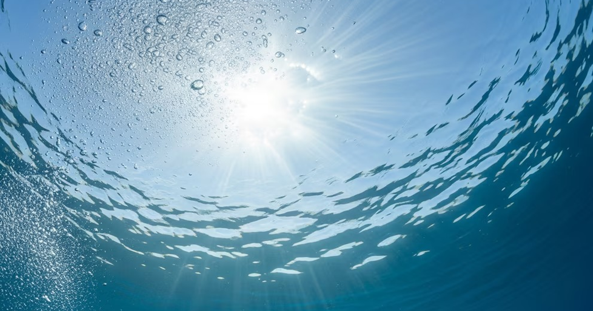 Vista bajo el agua con luz solar reflejada en la superficie, burbujas y un aura de frescura.