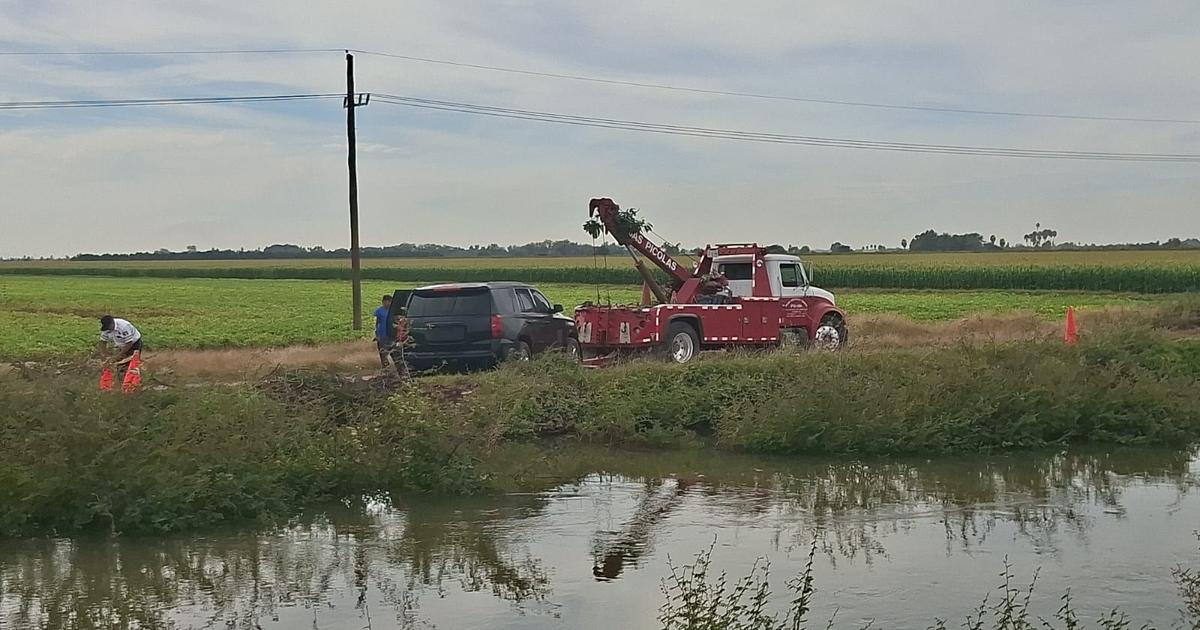 Rescate de vehículo negro por camión de remolque rojo en campo verde, Sinaloa.