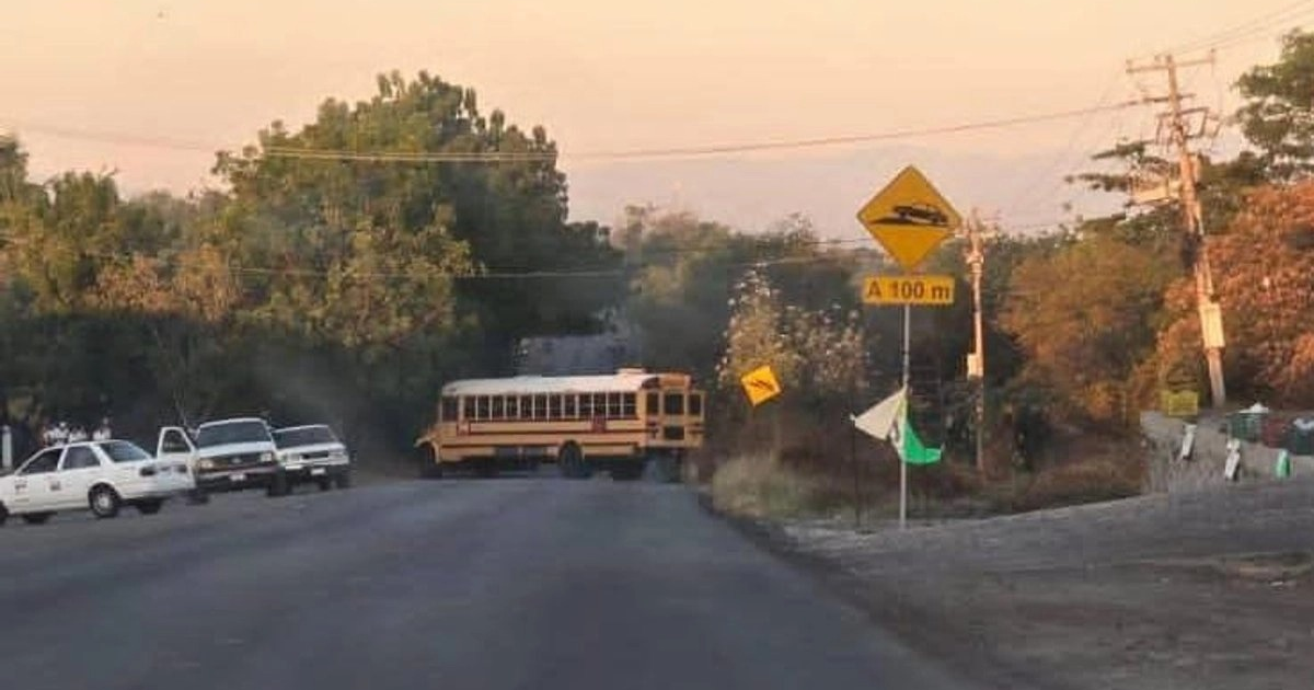 Autobús escolar detenido en carretera de Michoacán durante el atardecer y vehículos en movimiento.