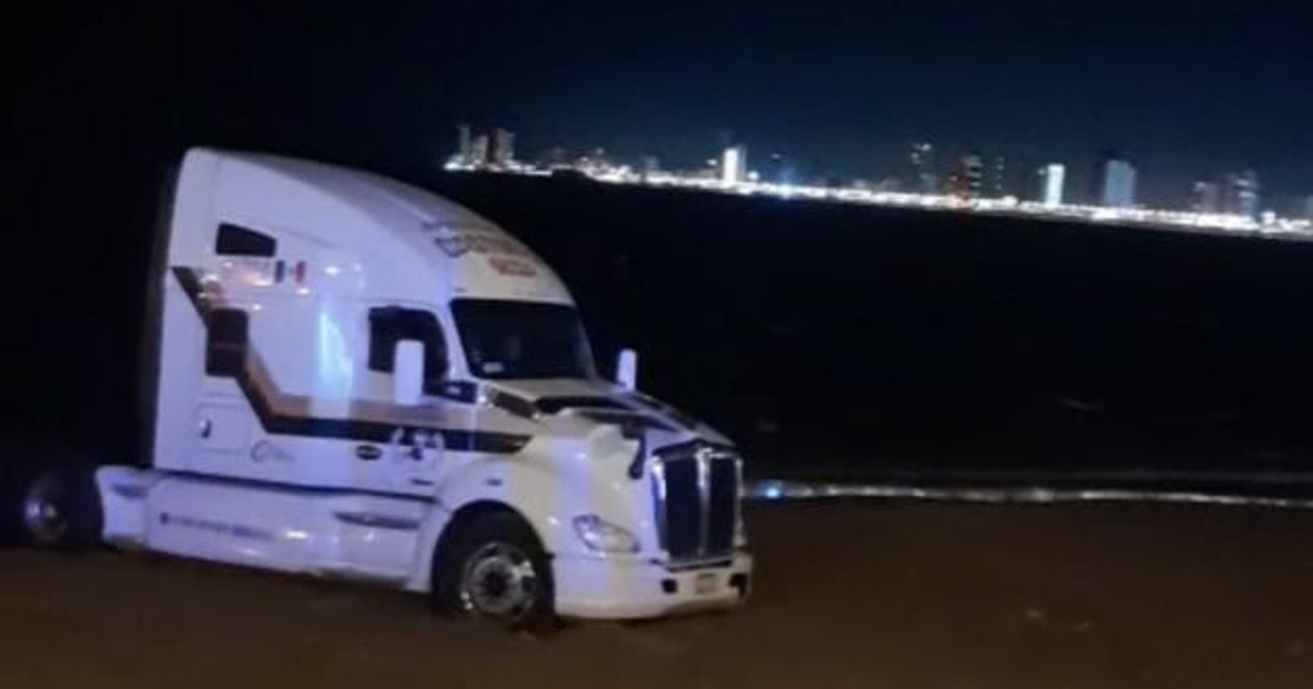 Camión atrapado en la playa de Mazatlán con ciudad de fondo