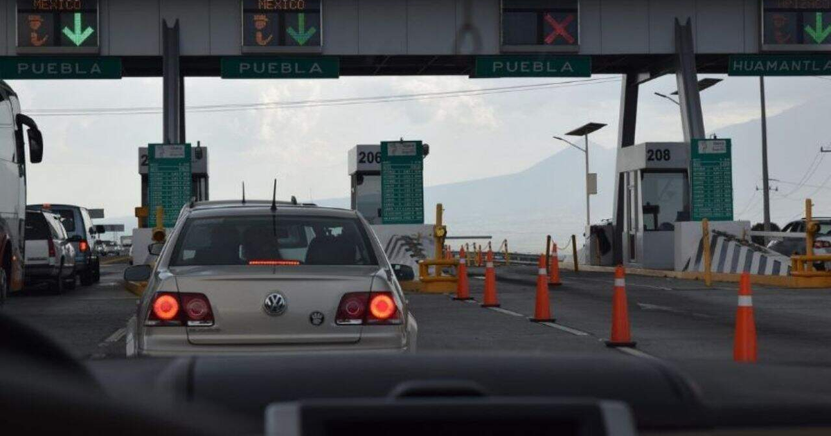 Autos en fila en un peaje mexicano con señales hacia Puebla y Huamantla y montañas al fondo.