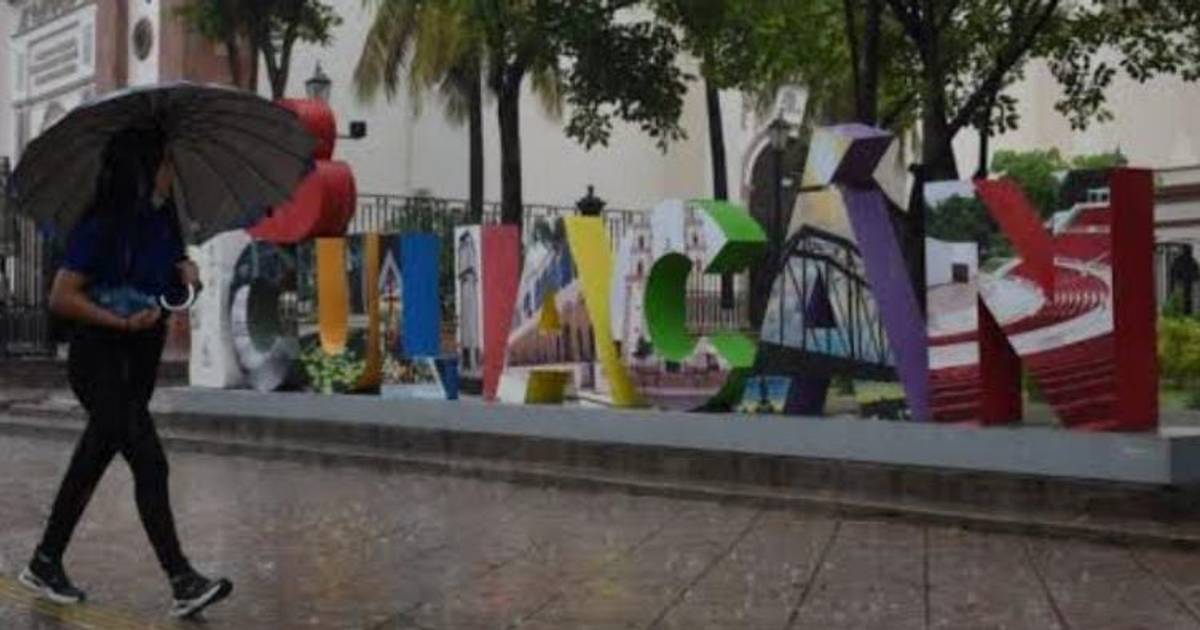 Persona con paraguas caminando frente a un letrero colorido de Culiacán en un día lluvioso.