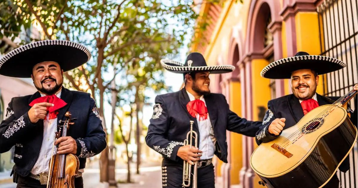 Tres músicos mariachis con trajes tradicionales mexicanos tocando sus instrumentos al aire libre.