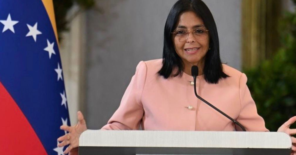 Mujer venezolana dando declaración desde un podio con bandera de Venezuela al fondo