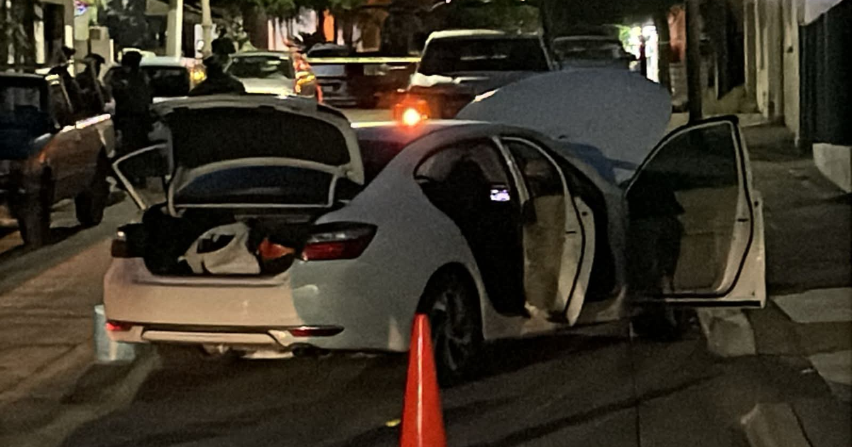 Automóvil Mazda 6 blanco con puertas abiertas y maletero abierto en escena nocturna urbana; cono de tráfico y personas alrededor.