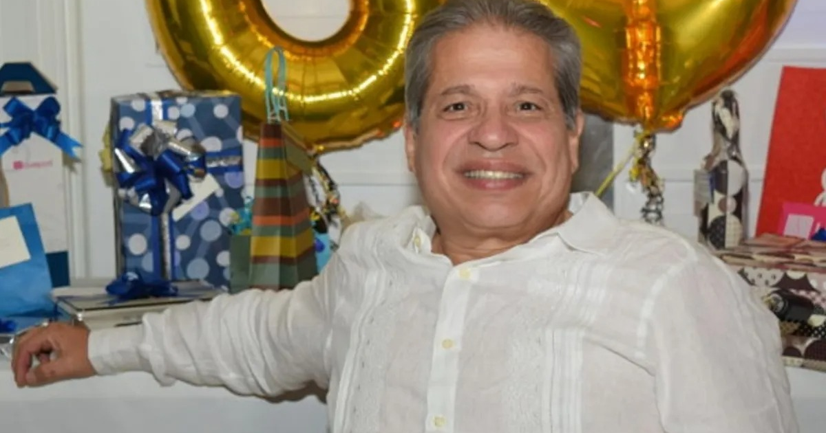Hombre sonriendo en una festividad con globos dorados y regalos, en honor a Gabriel Coppel Kelly.