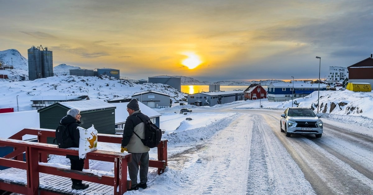 Un paisaje invernal con nieve en el que se ven personas en un puente, al atardecer sobre el agua, en Groenlandia.