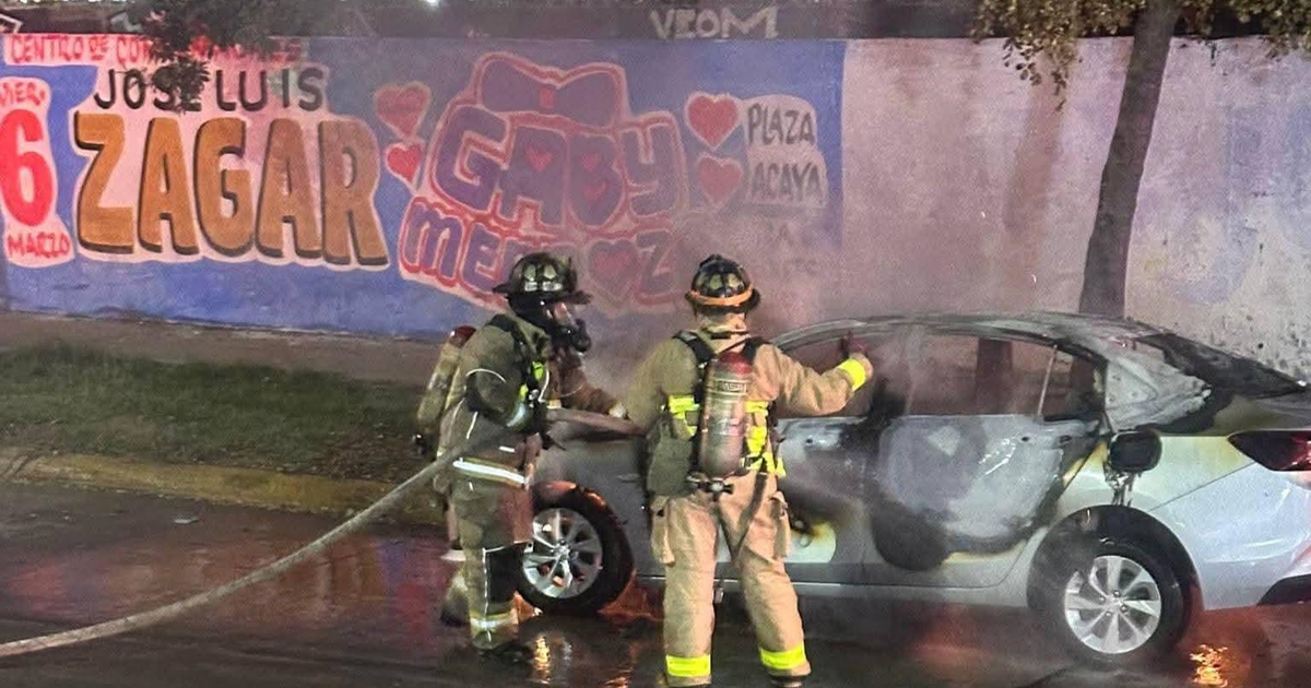 Dos bomberos extinguiendo un incendio de automóvil con una manguera, murales en la pared de fondo.