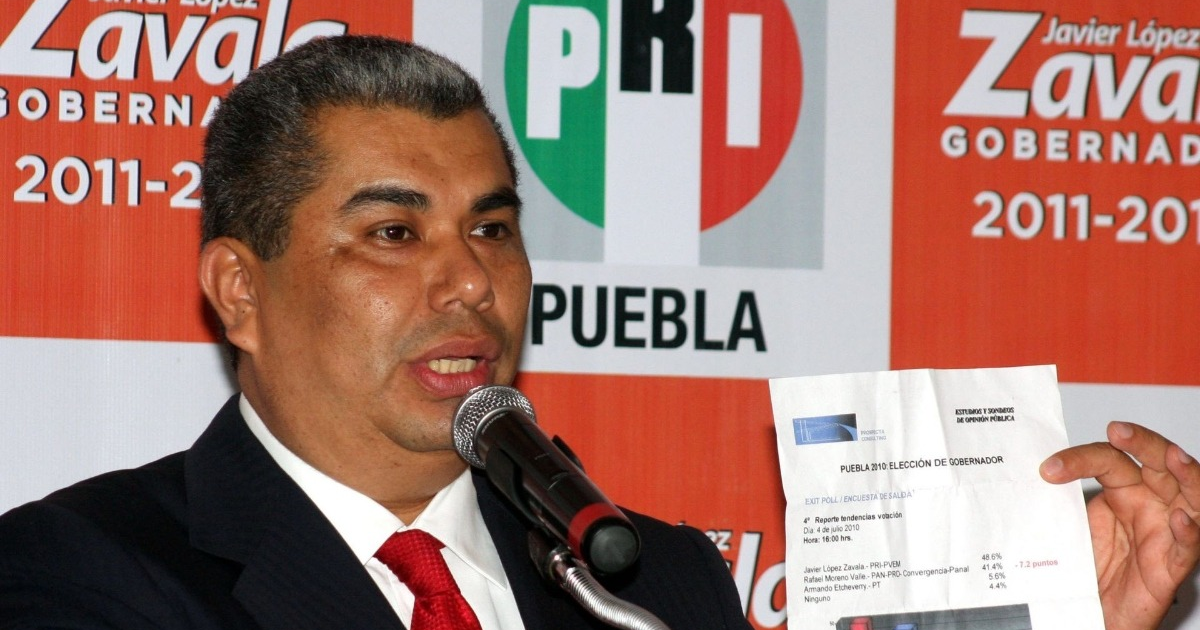 Hombre en conferencia de prensa del PRI sosteniendo un documento electoral