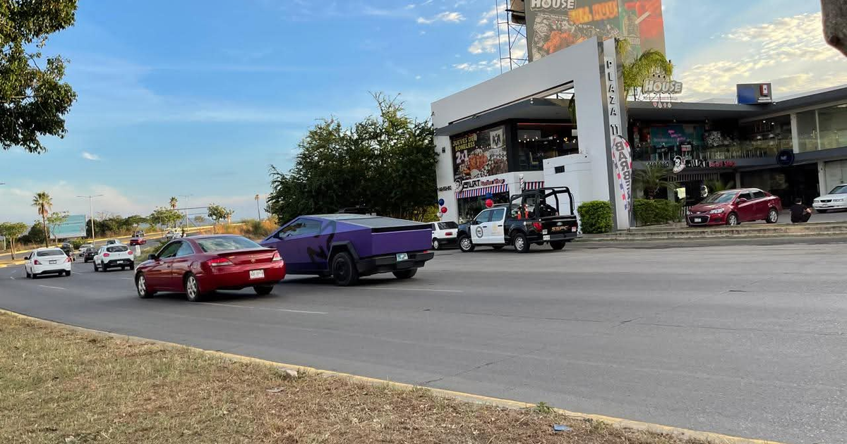 Tráfico urbano en Culiacán con automóviles de diversos colores, incluidas una Cybertruck morada y un edificio comercial a la derecha.