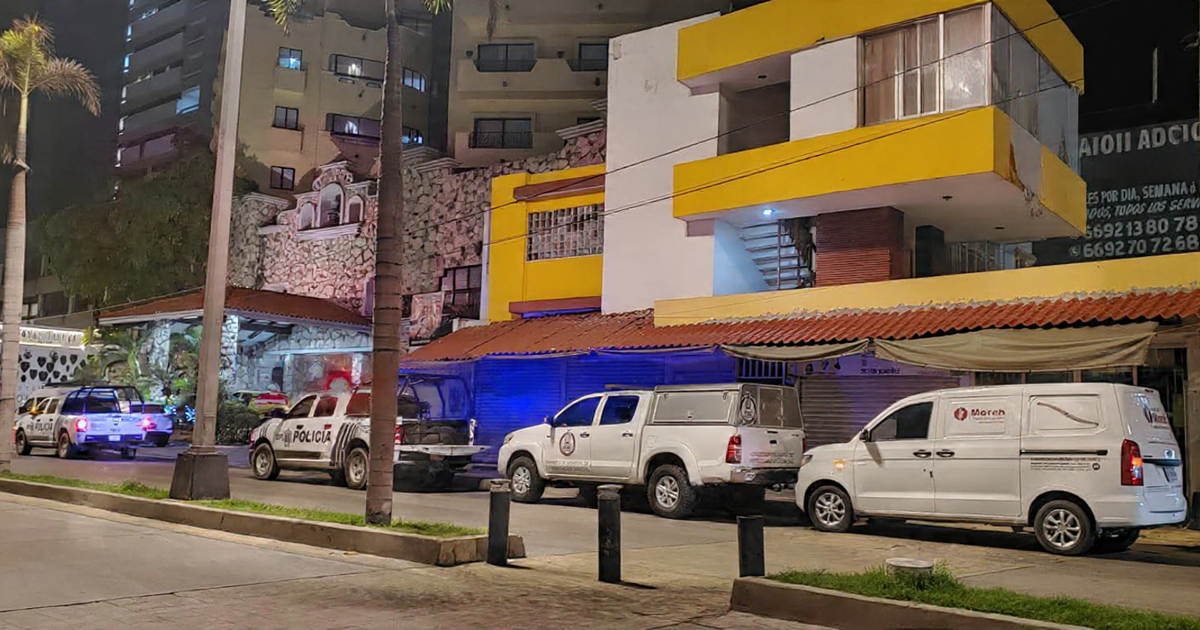 Fotografía nocturna de calle en Mazatlán con vehículos de policía estacionados, edificio amarillo y palmera visible.