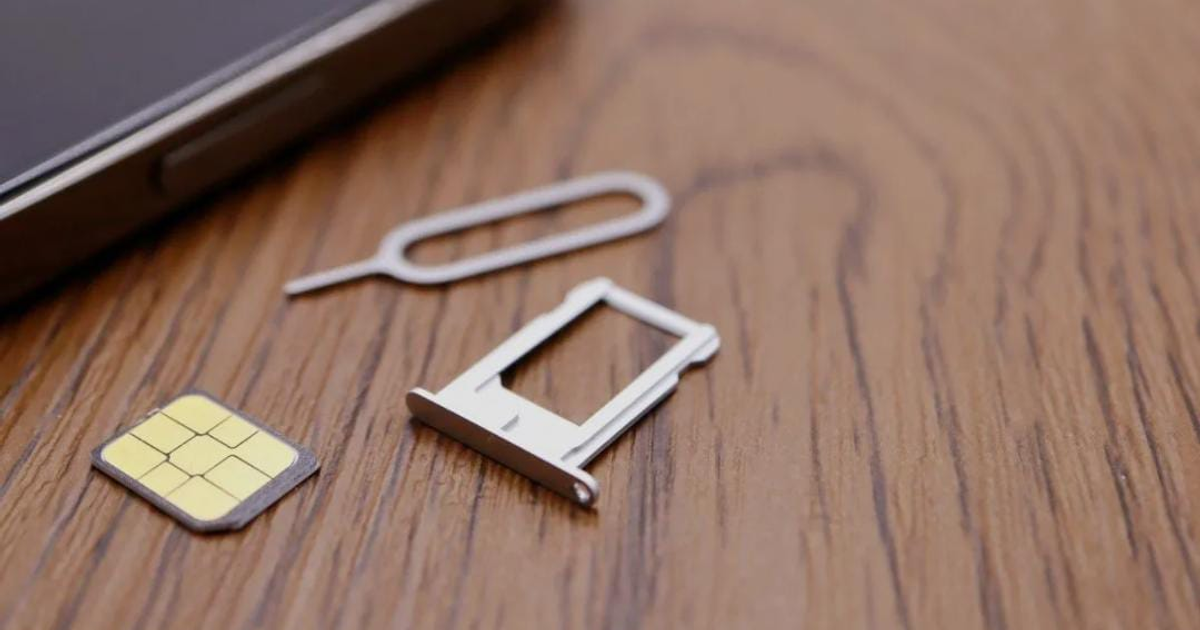 Tarjeta SIM, soporte y herramienta de extracción sobre superficie de madera con teléfono móvil en el fondo