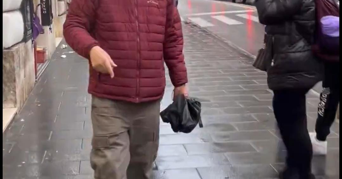 Hombre con chaqueta burdeos caminando en acera húmeda, posiblemente relacionado con un incidente con senador en la Roma, CDMX.