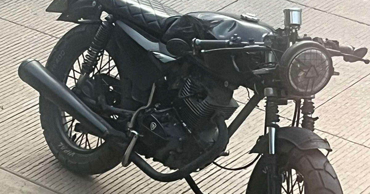 Motocicleta negra café racer con diseño minimalista y modificaciones, estacionada sobre pavimento.