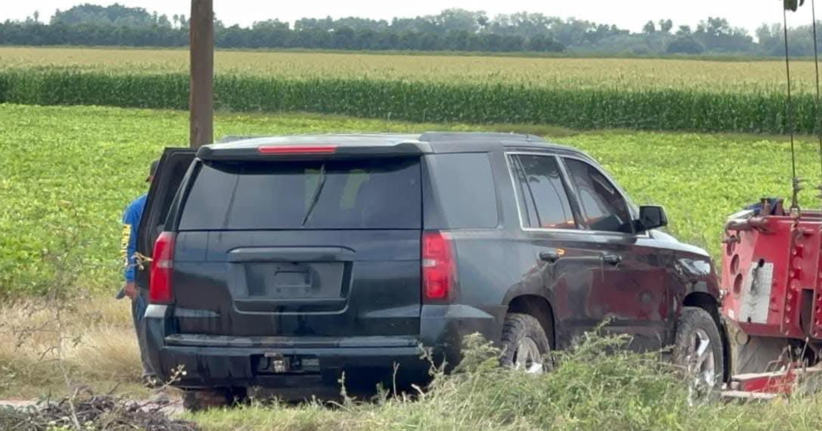 Chevrolet Tahoe negra estacionada con campos verdes y maquinaria agrícola en el fondo en área rural.