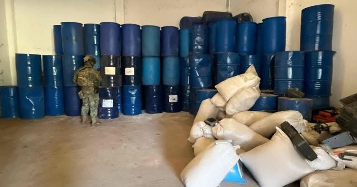 Interior de narcolaboratorio con barriles azules y personal de seguridad