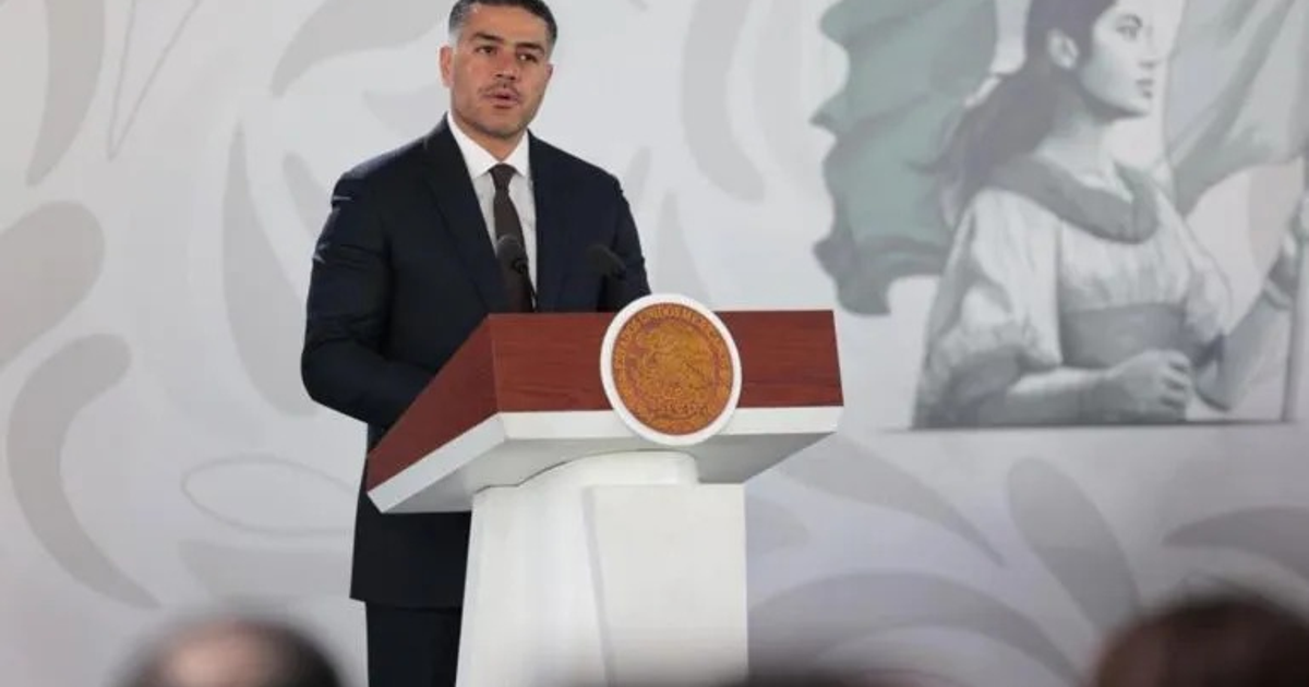 Hombre en conferencia de prensa junto a podio.