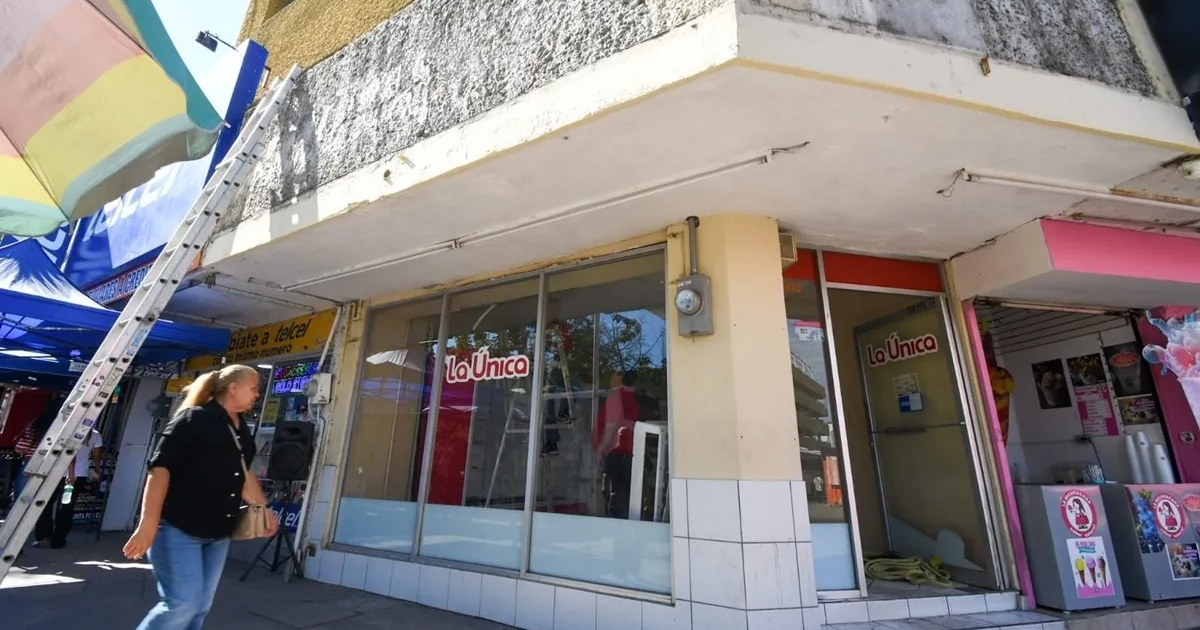 Fachada de 'La Única' con mujer caminando y toldos coloridos, simbolizando el cierre de un comercio emblemático en Culiacán.