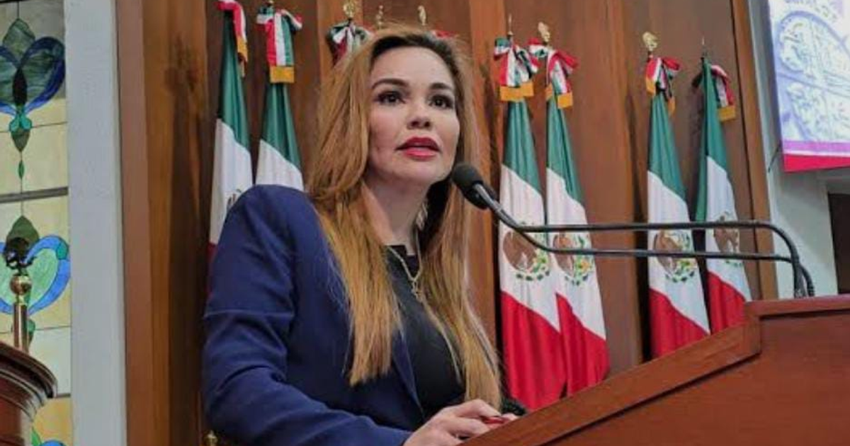 Diputada Paola Gárate Valenzuela hablando en un podio durante un evento público con banderas de México en el fondo.