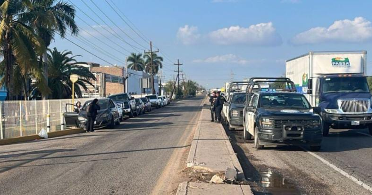 Imagen de una calle en Culiacán con vehículos de policía y personas, tras persecución y operativo de seguridad.